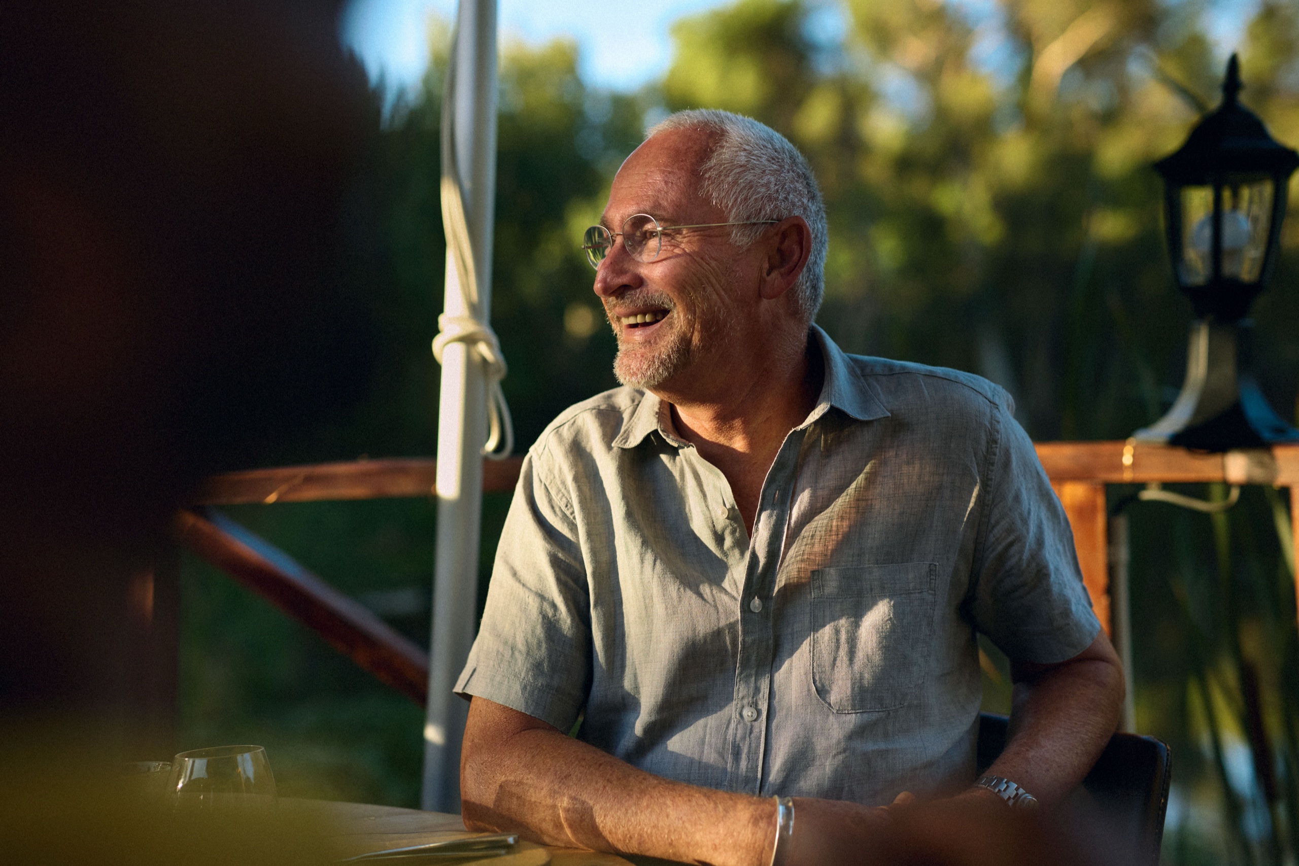 A guest laughs at the table in warm evening light, wine glass in the foreground