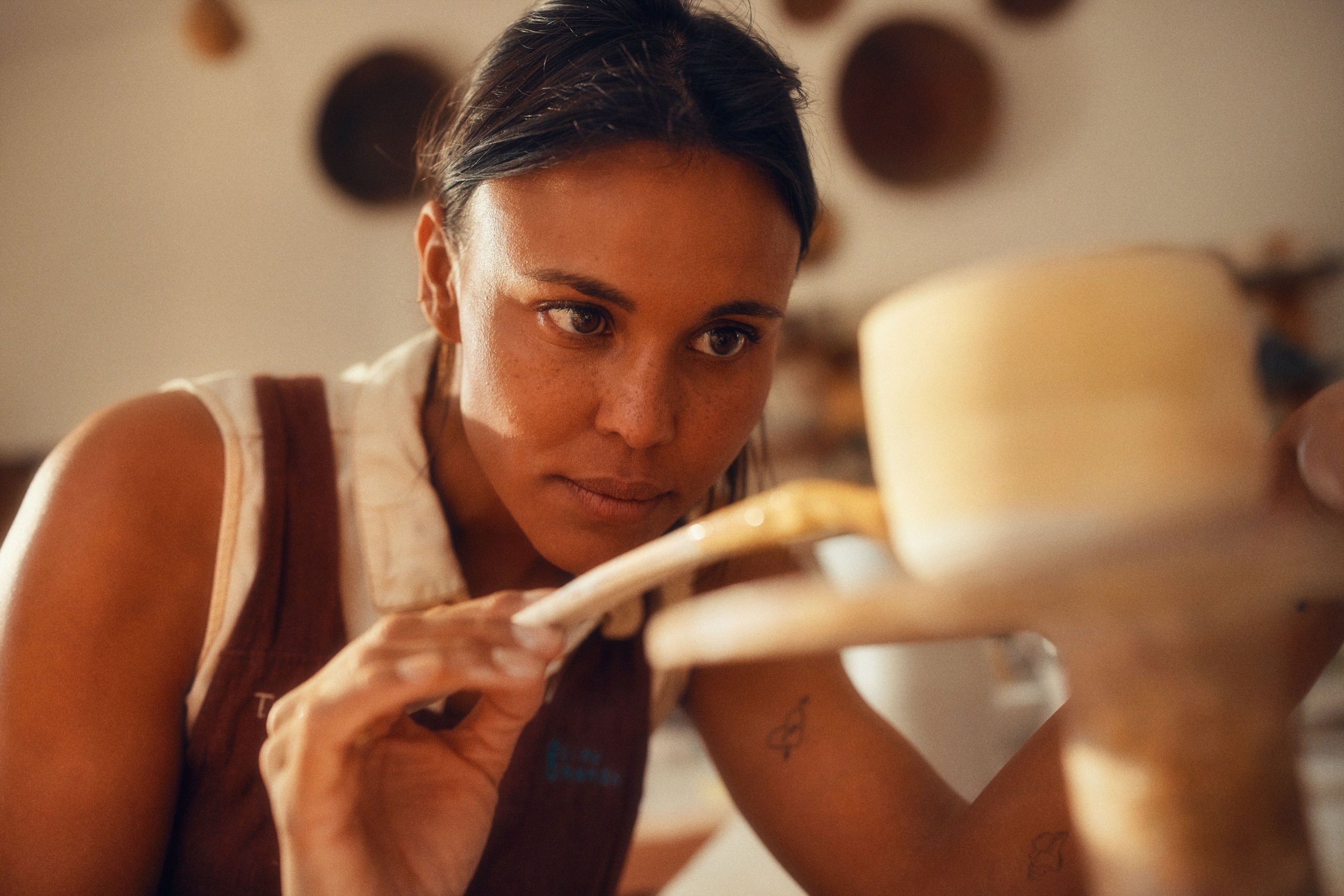 A ceramicist trims a pot, focused in warm side light